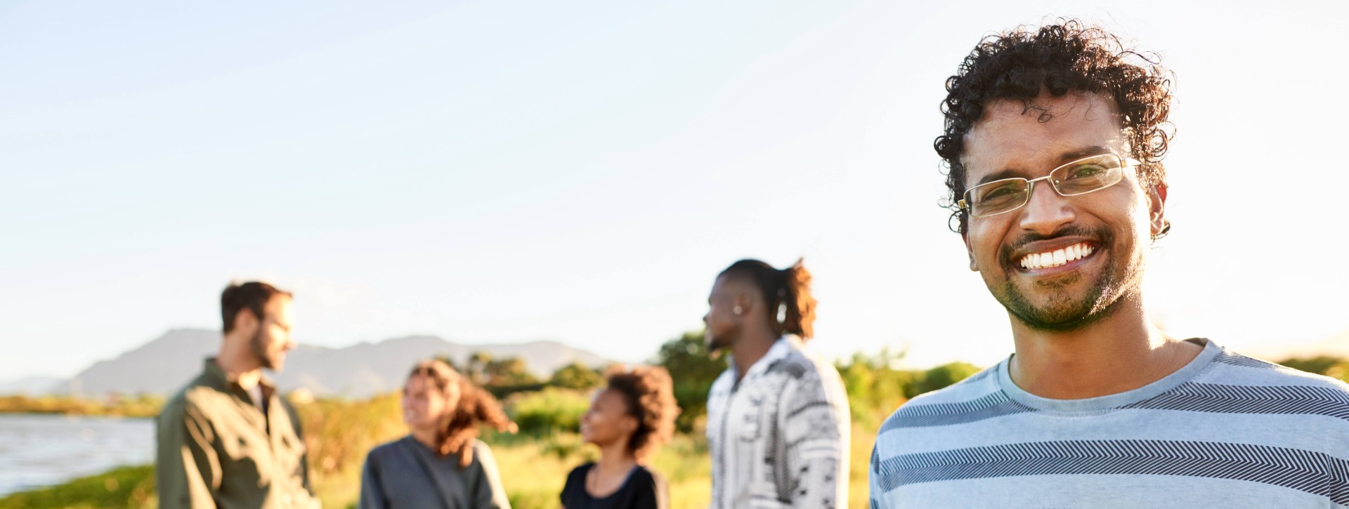 Man wearing glasses outside smiling at camera with group of friends in background
