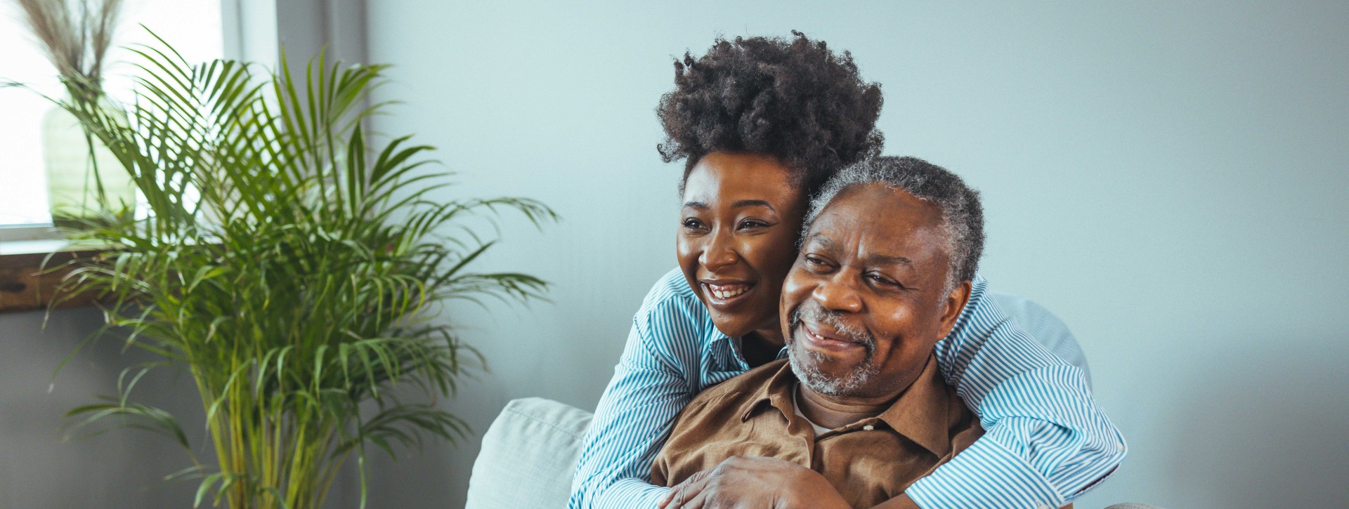 Daughter hugging her father from behind while he sits on couch